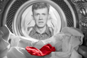 Red sock in white washing load with concerned man staring into washing machine